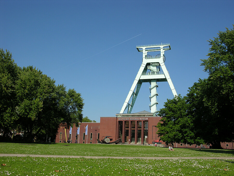 Außenansicht des Deutschen Bergbau-Museums Bochum mit Förderturm im Hintergrund und Blumenwiese im Vordergrund.